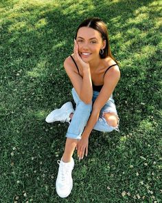 a woman sitting in the grass with her hand on her chin and looking at the camera