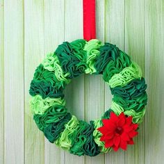 a green wreath with red flowers hanging on a wooden wall next to a red ribbon