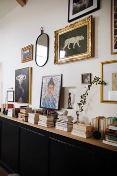 there are many framed pictures on the wall and books on the long table in front of them