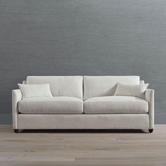 a white couch sitting on top of a hard wood floor next to a gray wall