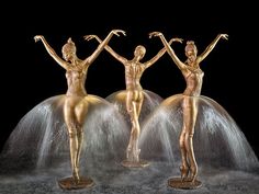 three gold statues standing on top of a fountain with their hands up in the air