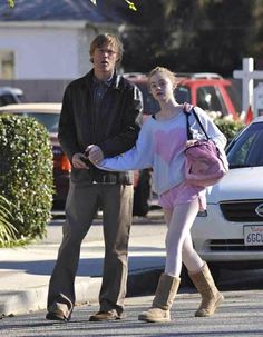 a man and woman walking down the street with cars in the backgrouds