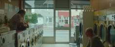 two people sitting at a table in front of washers and dryers with doors open