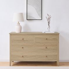 a white vase sitting on top of a wooden dresser next to a framed photograph and lamp