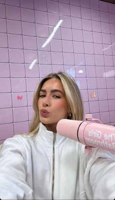 a woman with blonde hair is holding a pink microphone in front of a tiled wall