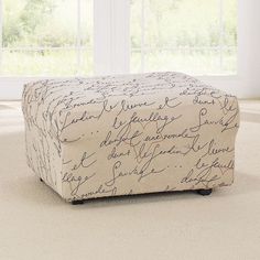 a white ottoman with writing on it in front of a large window and windowsill