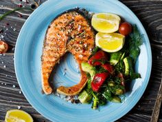 a blue plate topped with salmon and vegetables next to a fork, knife and spoon