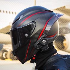 a person wearing a black helmet with red lines on the side and an airplane in the background