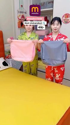 two people standing next to each other holding up shirts in front of a yellow table