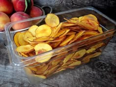 two plastic containers filled with sliced peaches next to other fruit on a wooden table