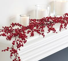 red berries and candles sit on a mantel