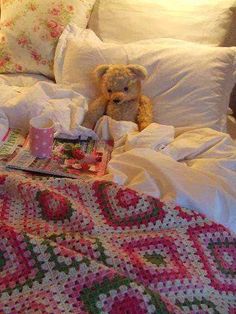 a teddy bear sitting on top of a bed next to a crocheted blanket