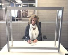 a woman sitting at a desk in front of a glass display case with papers on it