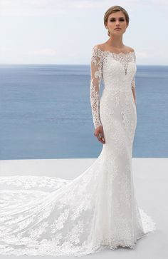 a woman in a white wedding dress standing on the beach with an ocean view behind her