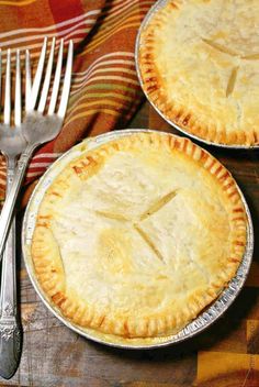 two pies sitting on top of a wooden table next to a fork and knife