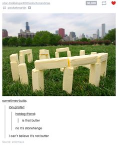 there is a bench made out of plastic blocks in the grass with buildings in the background