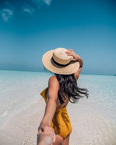 a woman in a yellow swimsuit and straw hat walks along the beach towards the ocean