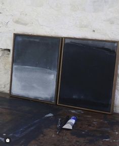 an empty chalkboard next to two windows on the ground with paint and a pen