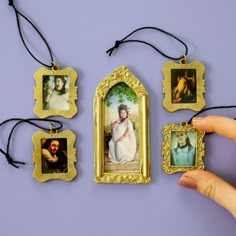 a hand is holding four framed pictures in front of a purple wall with black string