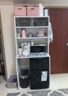 a microwave oven sitting on top of a white shelf next to a black refrigerator freezer