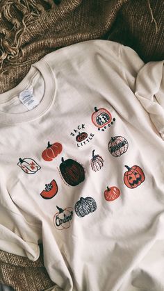 a white t - shirt with pumpkins on it is laying on a brown blanket