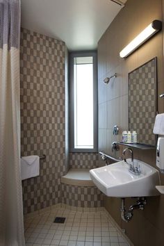 a bathroom with checkered walls and tile flooring is pictured in this image, there is a window above the sink