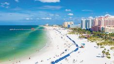 the beach is crowded with people and buildings in the distance, along with blue water