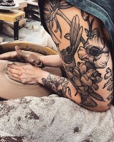 a woman is working on a pottery wheel with flowers and leaves tattooed on her leg