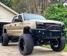 a tan truck parked in front of a house with large tires on it's wheels