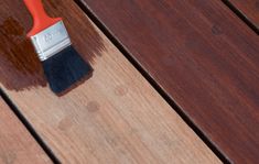 a red paint brush sitting on top of a wooden table next to a brown stain