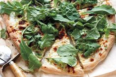 a pizza topped with greens on top of a wooden cutting board next to a spatula