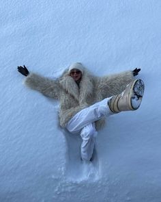 a person laying in the snow with their legs spread out and arms outstretched, wearing white pants