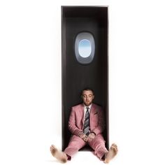 a man in a pink suit and tie is sitting inside an airplane shaped box with his feet up