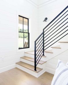 there is a white staircase with black railing and wood flooring in the room next to the window