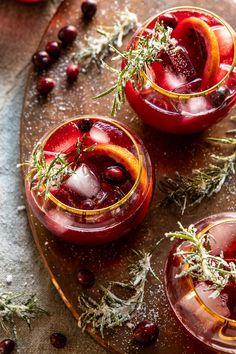 two glasses filled with red liquid and garnished with herbs on a wooden tray