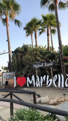 a sign that says i love marbella with palm trees in the background and a large red heart on it