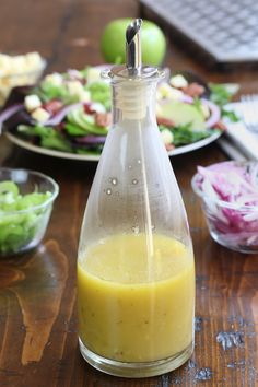 a bottle filled with dressing sitting on top of a wooden table next to plates of salad