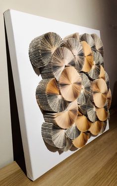 an art piece made out of folded books is displayed on a wooden floor in front of a white wall