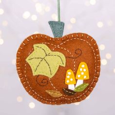 an apple ornament hanging from a string with leaves and mushrooms in the center