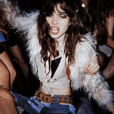 a woman sitting on the ground with her arms around her body and wearing a fur coat