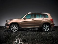 a brown car parked on top of a dirt field next to a black wall and floor