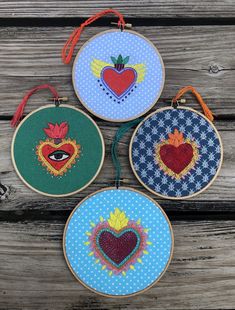 three hand embroidered hoops with hearts and eyes on them, hanging from wooden boards