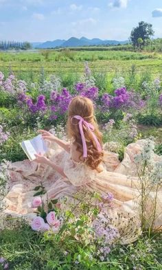 a woman sitting in the middle of a field with purple flowers and holding a book