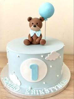 a blue cake with a teddy bear on top and a balloon in the air above it