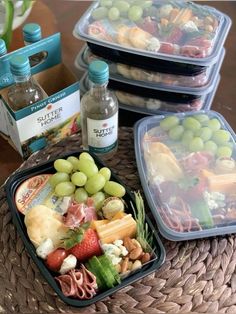 three plastic containers filled with food on top of a wicker table next to bottles of water