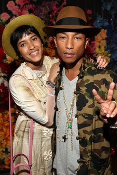 a man and woman standing next to each other in front of a floral wall with flowers