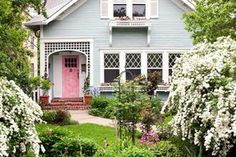 a blue house with pink door surrounded by trees and flowers in the front yard area