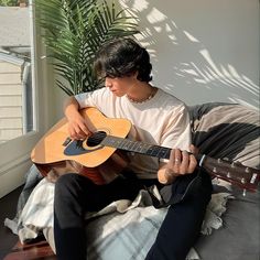 a young man sitting on top of a bed holding an acoustic guitar in his hands