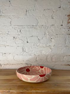 a bowl sitting on top of a wooden table next to a white brick wall and wood floor