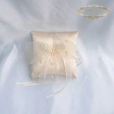 a white ring pillow with pearls on the front and ribbon at the back, sitting on a bed